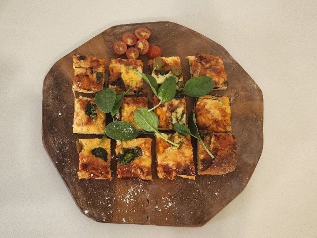 Sliced vegetable pizza served on a wooden board with greens on top.